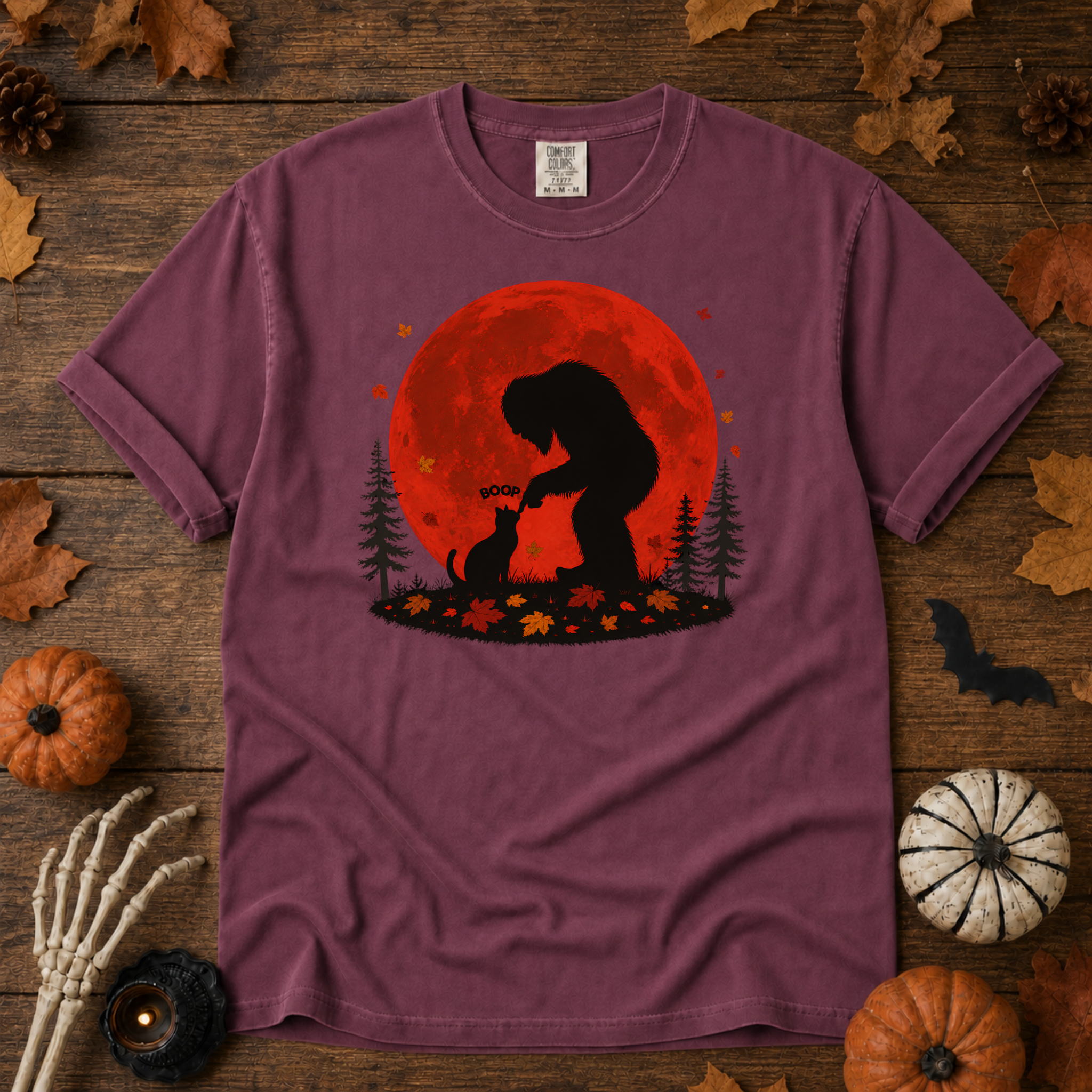 Berry Comfort Colors t-shirt featuring Bigfoot booping a black cat's nose in front of a red autumn moon, with maple leaves and pine trees, Trail & Ember Co.