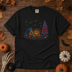 Black Comfort Colors t-shirt featuring a neon-lit Halloween campsite scene — glowing tent, jack-o'-lantern on a stump, pine tree, bats and stars in red, blue, and gold, Trail & Ember Co.