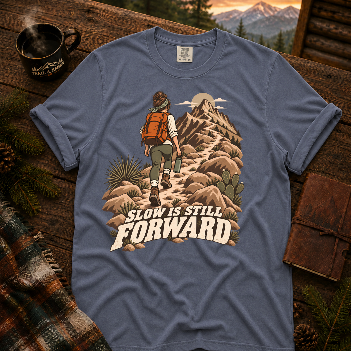 Slow is Still Forward hiking t-shirt in Blue Jean — hiker with an orange pack climbing a desert ridge trail, on garment-dyed Comfort Colors 1717, Trail & Ember Co.
