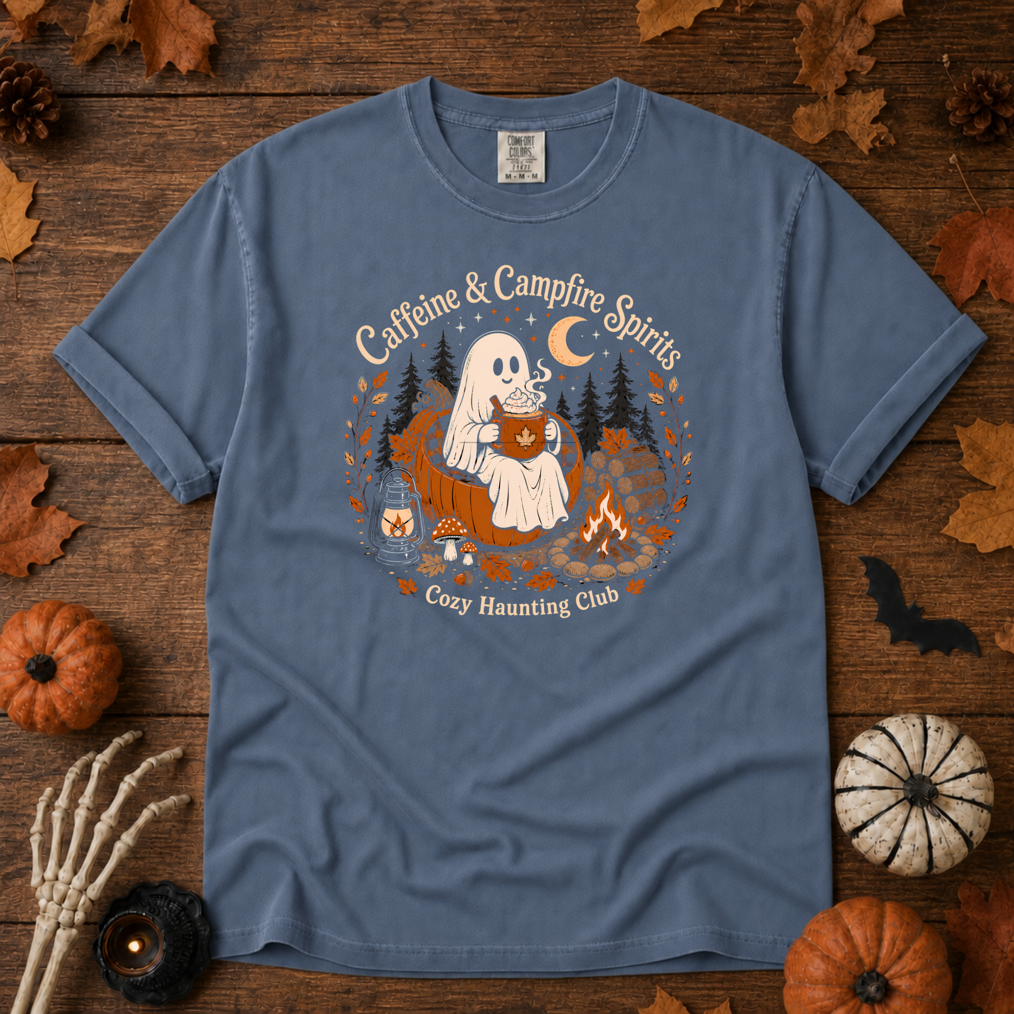 Blue Jean Comfort Colors t-shirt featuring a ghost sitting in a pumpkin chair with a steaming mug of cocoa, campfire, lantern, mushrooms and maple leaves, Trail & Ember Co.