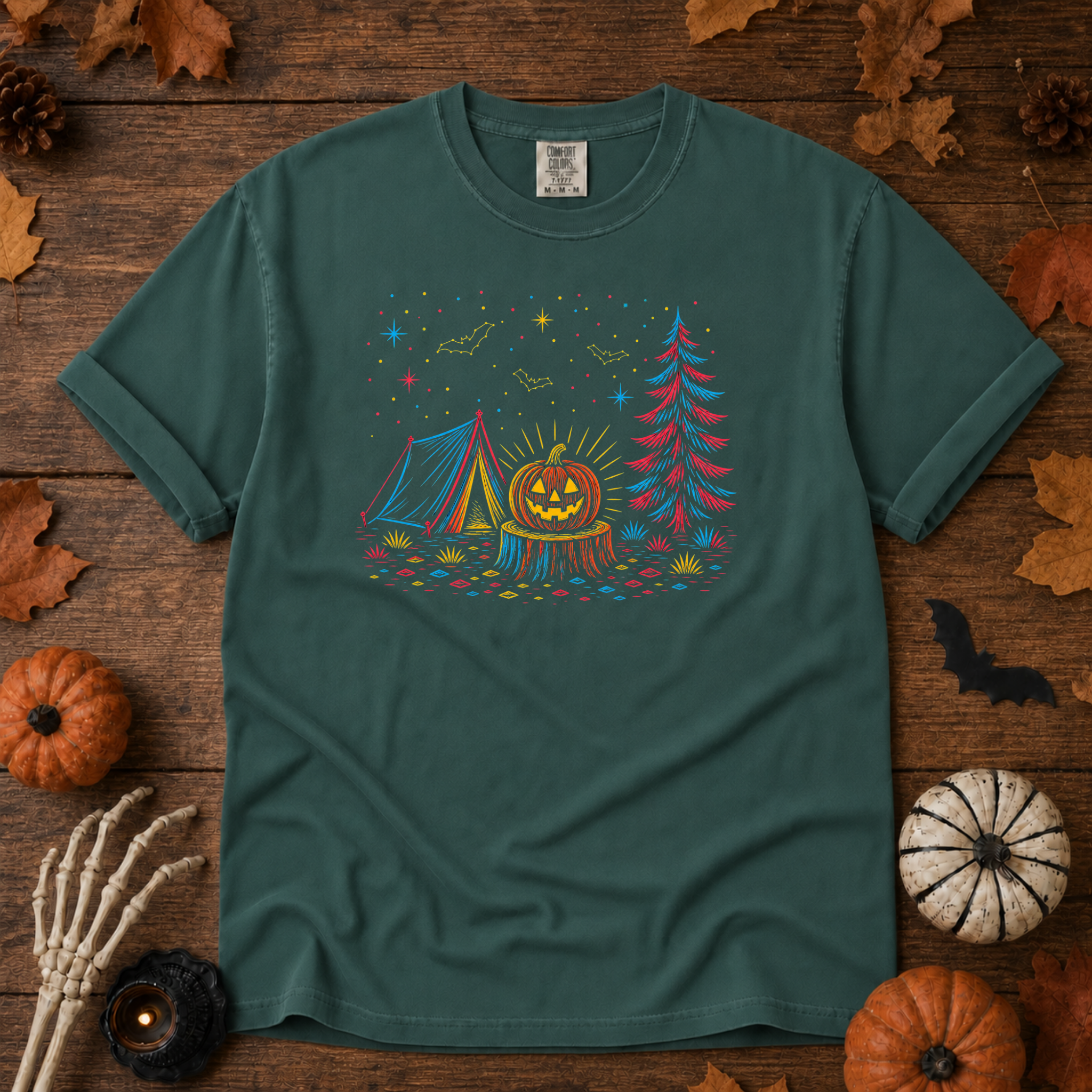 Blue Spruce Comfort Colors t-shirt featuring a neon-lit Halloween campsite scene — glowing tent, jack-o'-lantern on a stump, pine tree, bats and stars in red, blue, and gold, Trail & Ember Co.