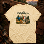 Butter yellow Comfort Colors t-shirt with a funny group hiking design — bluebird, frog, cardinal, rabbit, fox, chick and raccoon on the trail under a We're All In This Together, Like Hostages headline