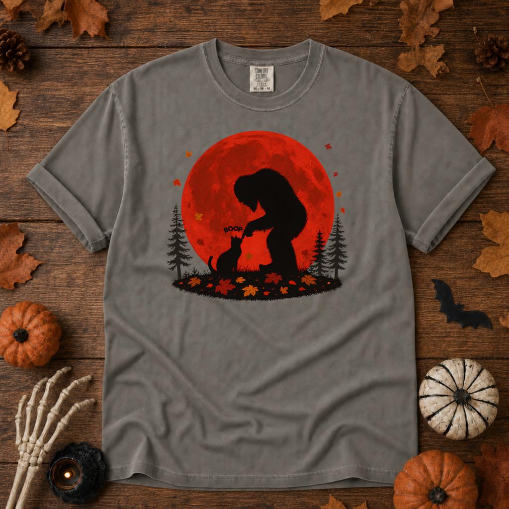Grey Comfort Colors t-shirt featuring Bigfoot booping a black cat's nose in front of a red autumn moon, with maple leaves and pine trees, Trail & Ember Co.