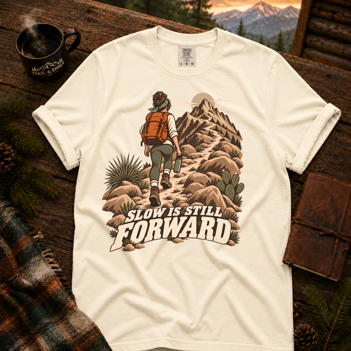 Slow is Still Forward hiking t-shirt in Ivory — hiker with an orange pack climbing a desert ridge trail, on garment-dyed Comfort Colors 1717, Trail & Ember Co.