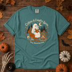 Seafoam Comfort Colors t-shirt featuring a ghost sitting in a pumpkin chair with a steaming mug of cocoa, campfire, lantern, mushrooms and maple leaves, Trail & Ember Co.