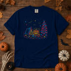 True Navy Comfort Colors t-shirt featuring a neon-lit Halloween campsite scene — glowing tent, jack-o'-lantern on a stump, pine tree, bats and stars in red, blue, and gold, Trail & Ember Co.