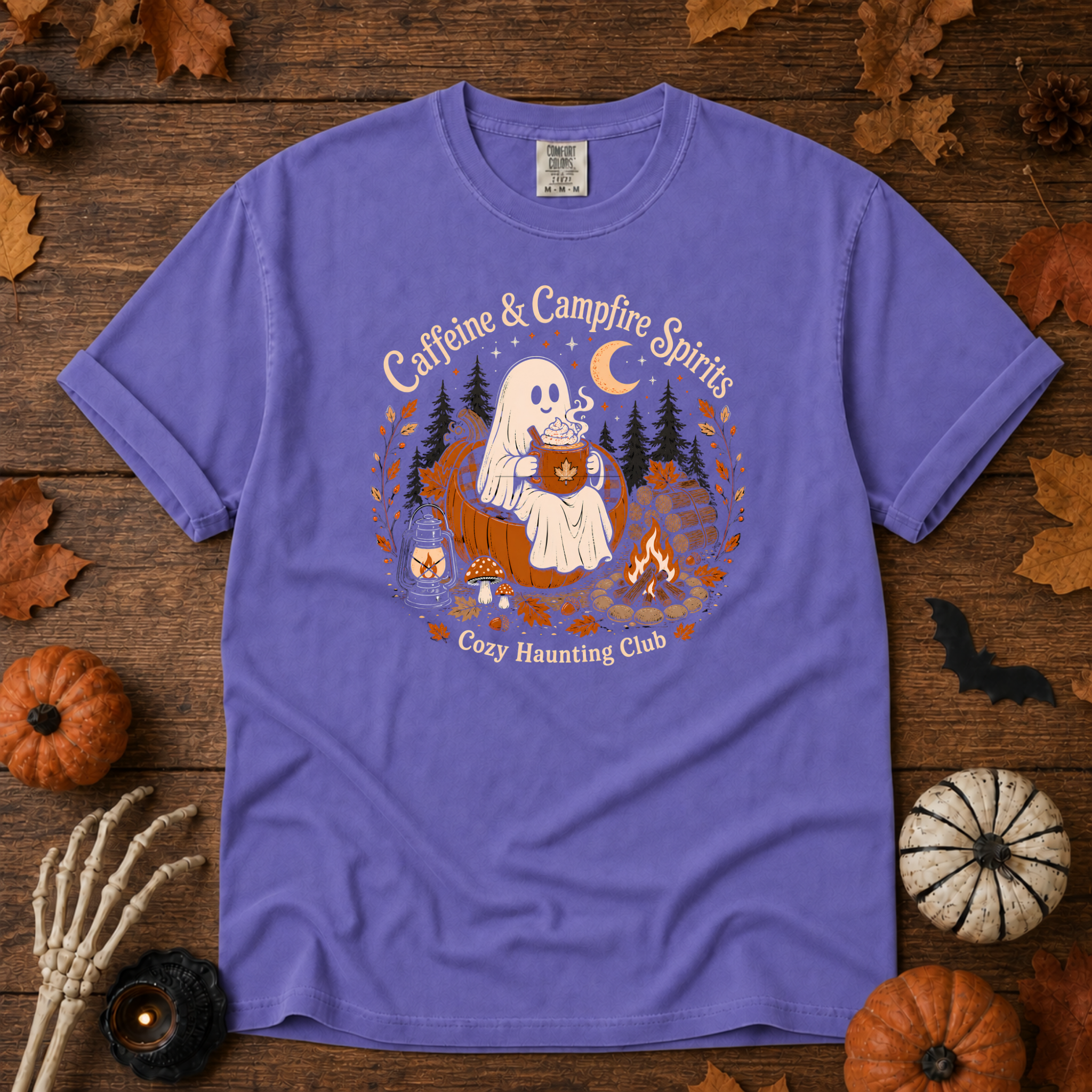 Violet Comfort Colors t-shirt featuring a ghost sitting in a pumpkin chair with a steaming mug of cocoa, campfire, lantern, mushrooms and maple leaves, Trail & Ember Co.