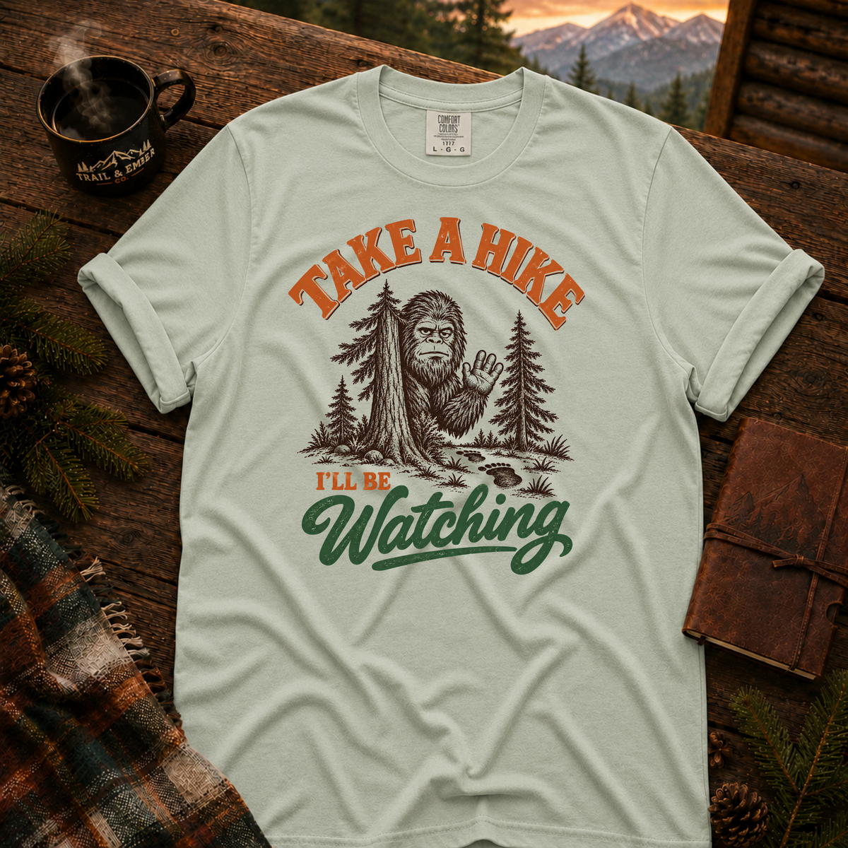 Bay Comfort Colors T-shirt with Take a Hike, I'll Be Watching Bigfoot waving behind a pine tree.