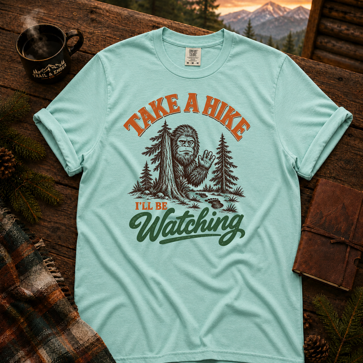 Chalky Mint Comfort Colors T-shirt with Take a Hike, I'll Be Watching Bigfoot waving behind a pine tree.