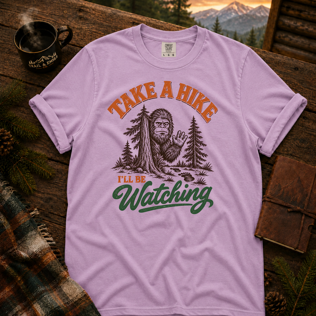 Orchid Comfort Colors T-shirt with Take a Hike, I'll Be Watching Bigfoot waving behind a pine tree.